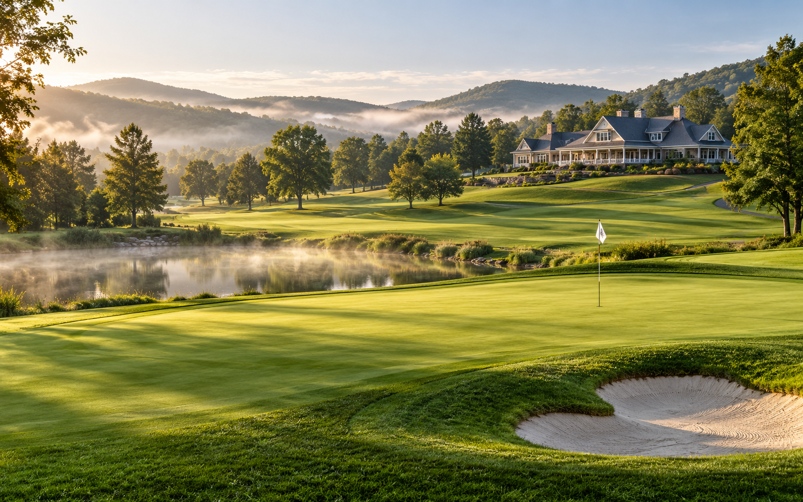 Golf course green beside a misty pond with the clubhouse on a hill at sunrise